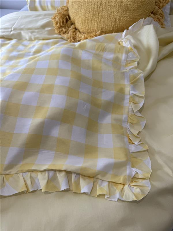 Yellow and white checkered blanket with ruffled edge on a bed.