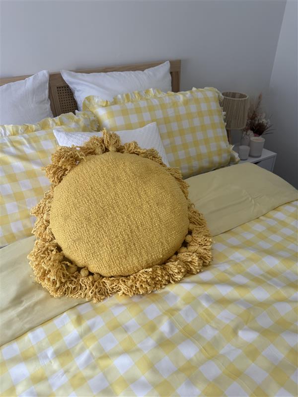 Yellow checkered bedding with a round knitted pillow on a bed.