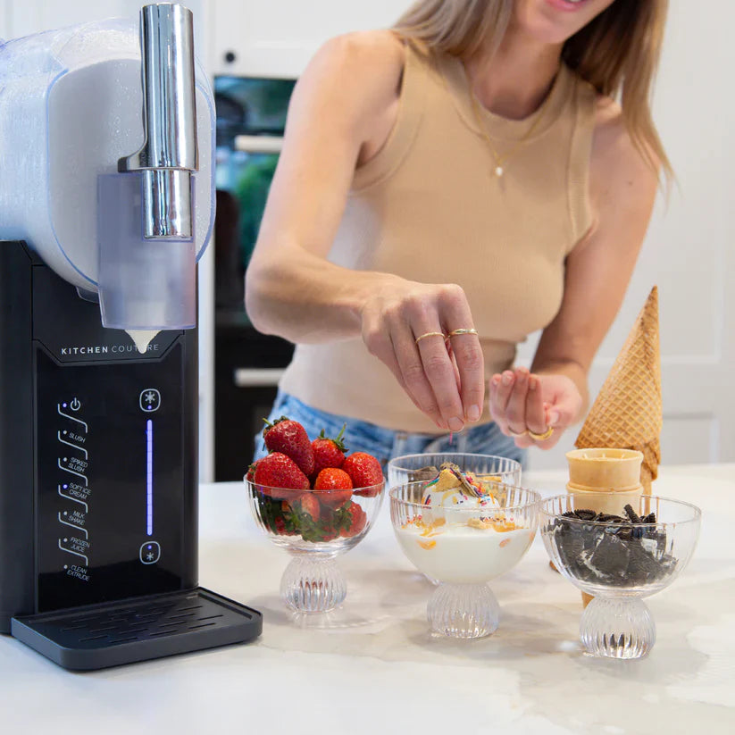 Person preparing a dessert with ice cream cones and bowls on a kitchen counter.