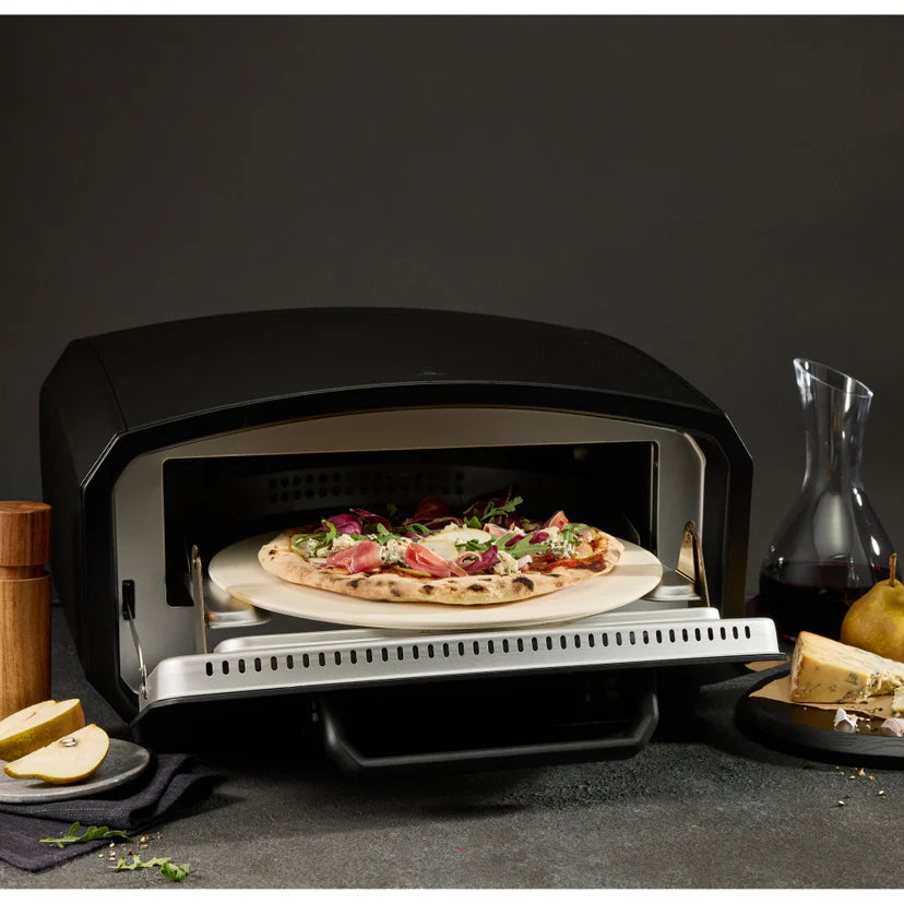 Black outdoor pizza oven with a pizza inside, surrounded by food items on a dark background