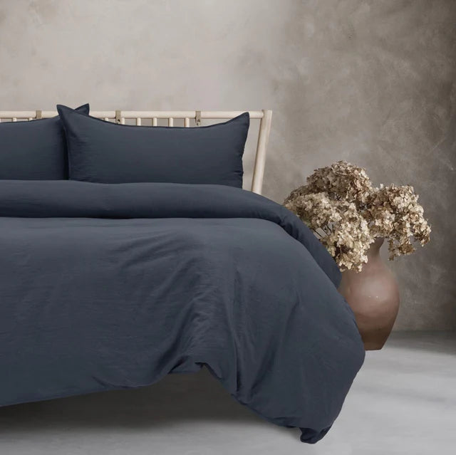 Navy blue bedding set on a bed with a vase of dried flowers on a gray surface.