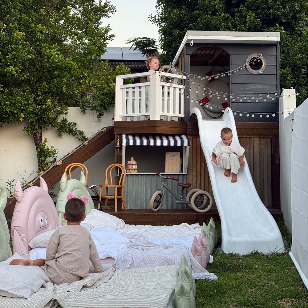 Children playing in a backyard with a playhouse, slide, and outdoor furniture.