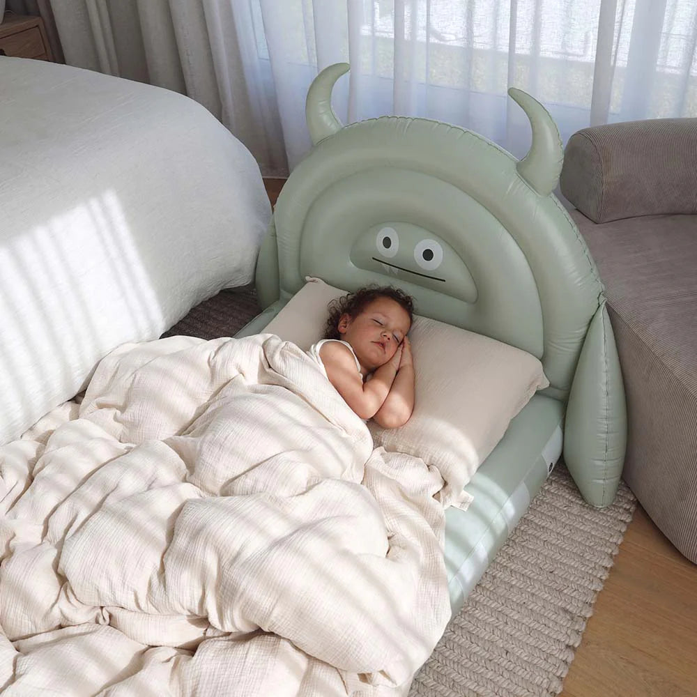 Child sleeping in a bed with a green inflatable monster headboard in a bedroom setting.
