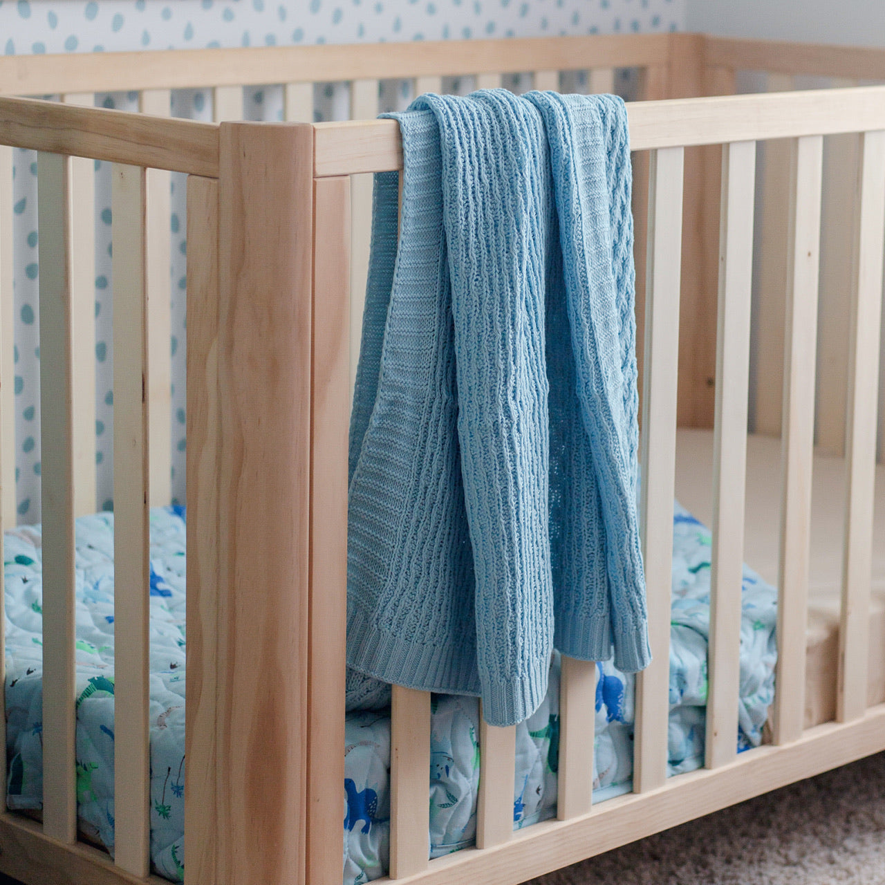 Lifestyle shot of Dinosaur Baby Blanket hanging over cot