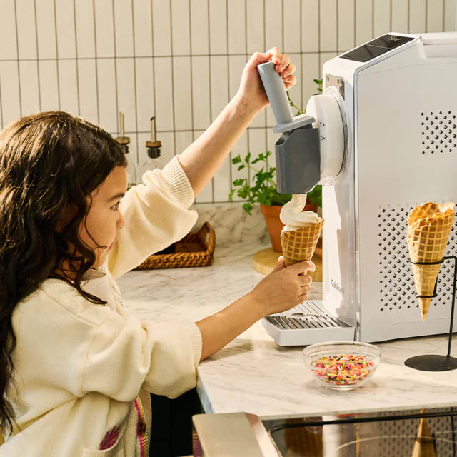 Woman using an ice cream machine to fill cones with ice cream.