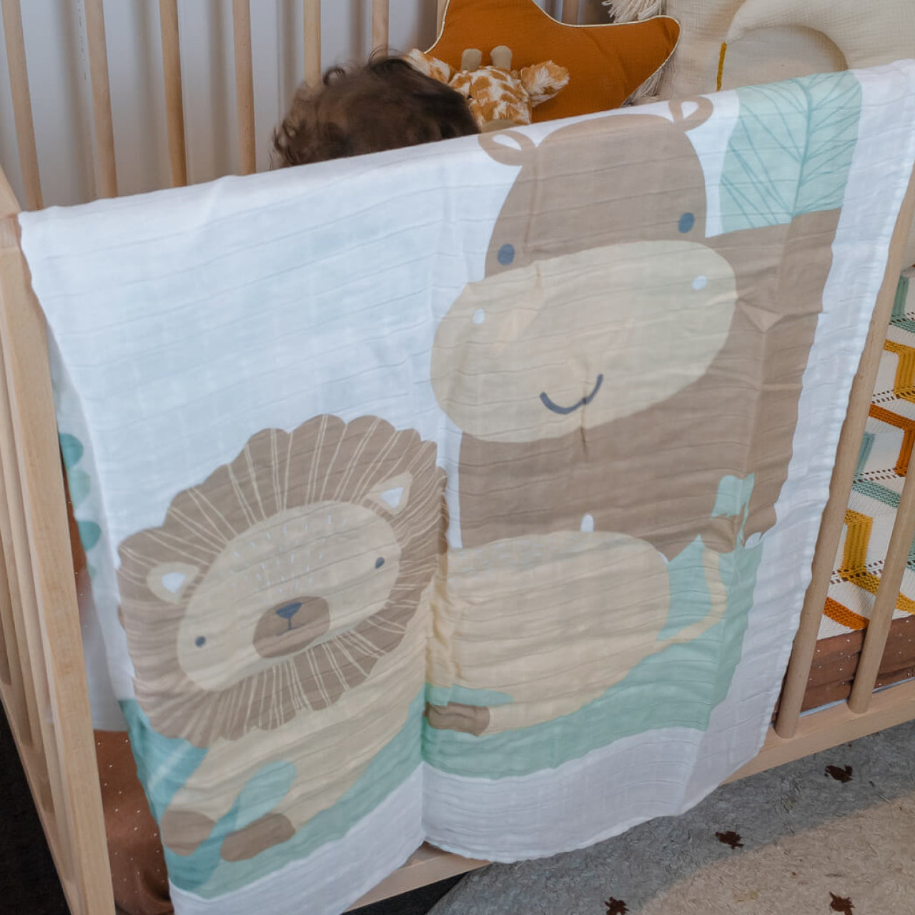 Lifestyle shot of Safari Muslin Blanket hanging over cot