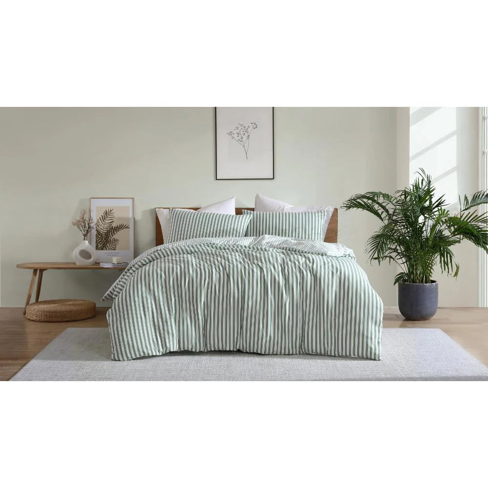Bed with green striped bedding in a bedroom setting with plants and decor.