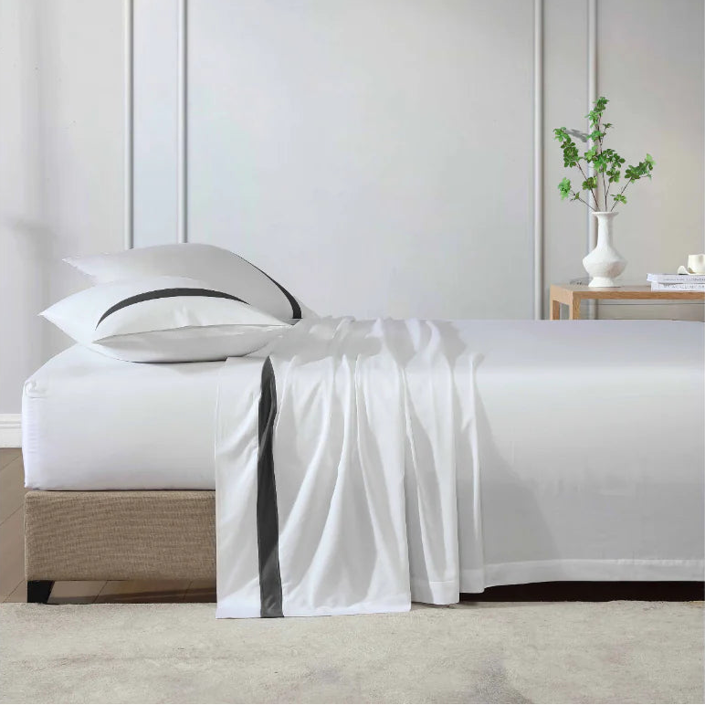 White bedspread on a bed in a bedroom setting with a vase of greenery on a nightstand.